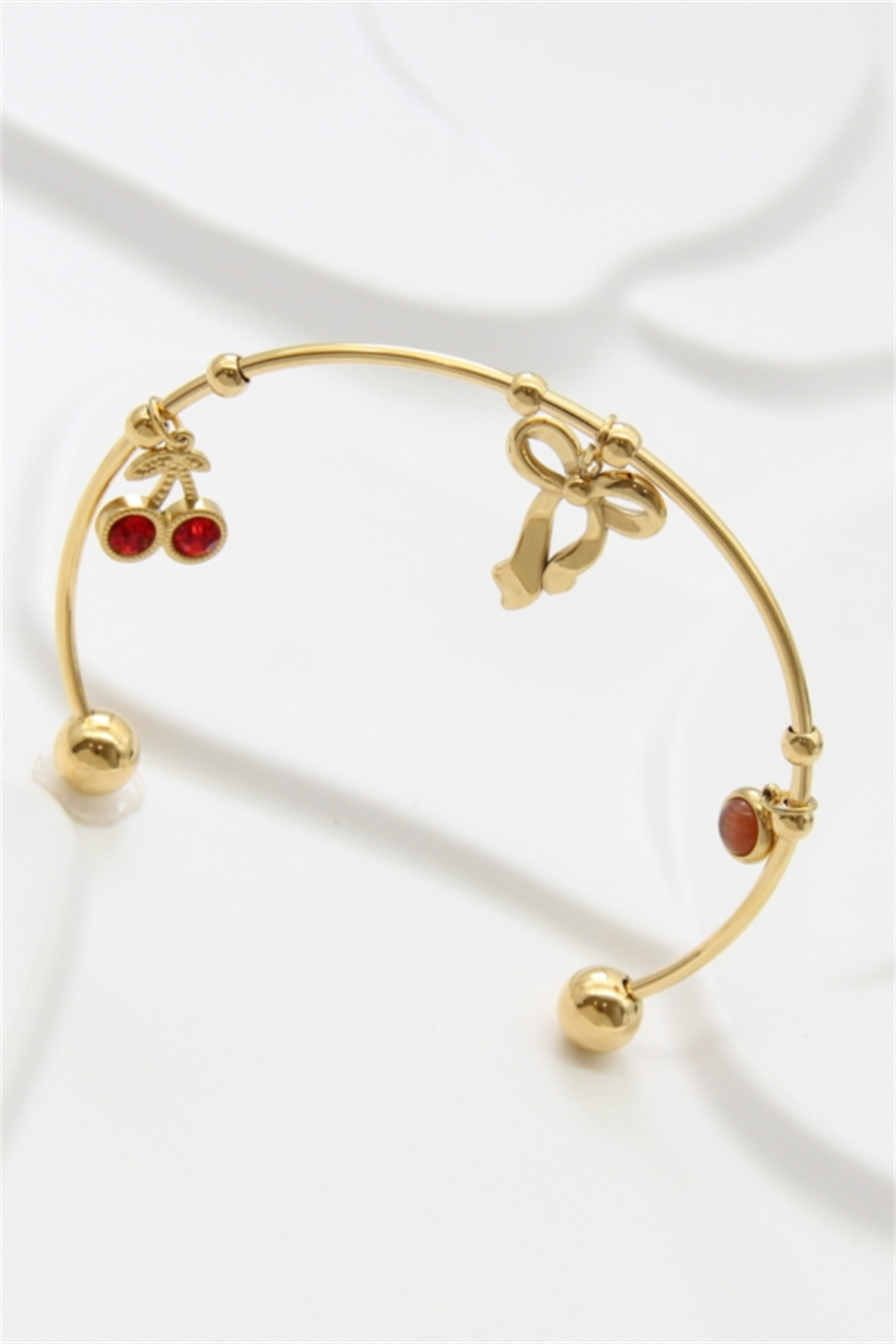 Mayorista Bellissima - Pulsera rígida con charms de acero inoxidable dorado – Nudo, cereza y piedra roja