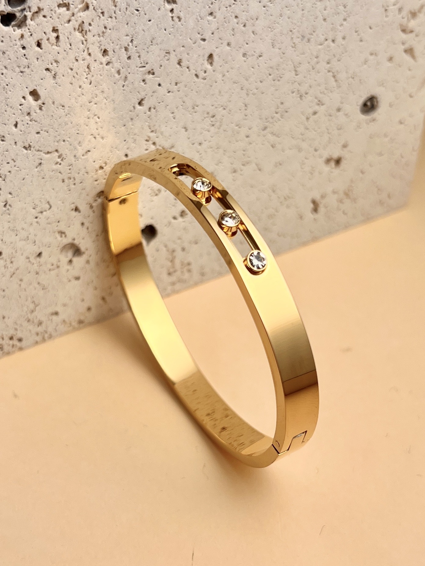 Grossista COSMOS - Bracciale rigido dorato in acciaio inossidabile da donna con cristallo scorrevole e tre pietre chiare, design elegante e chic