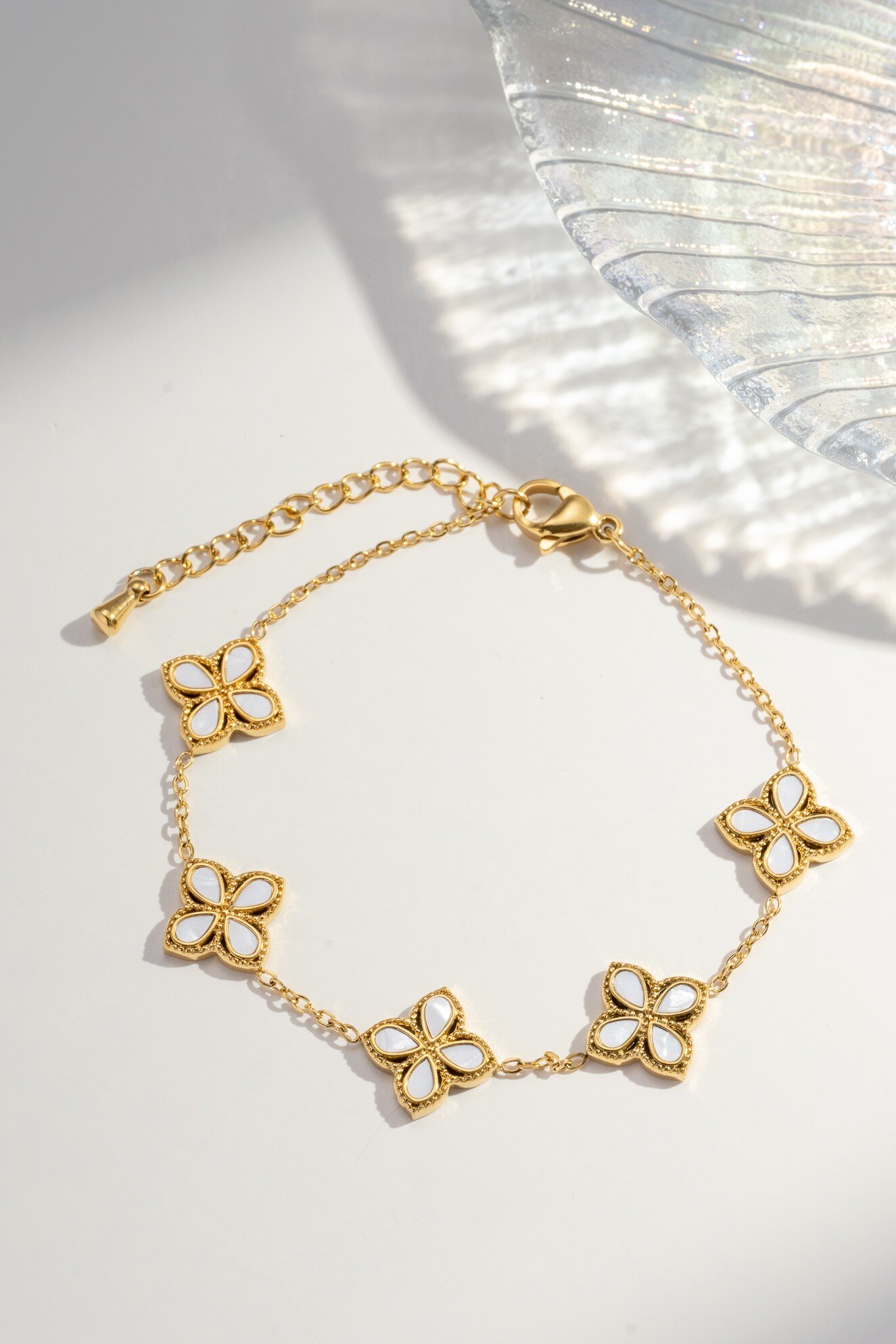 Wholesaler COSMOS - Women's gold stainless steel bracelet with five white mother-of-pearl petal flowers, adjustable elegant chain