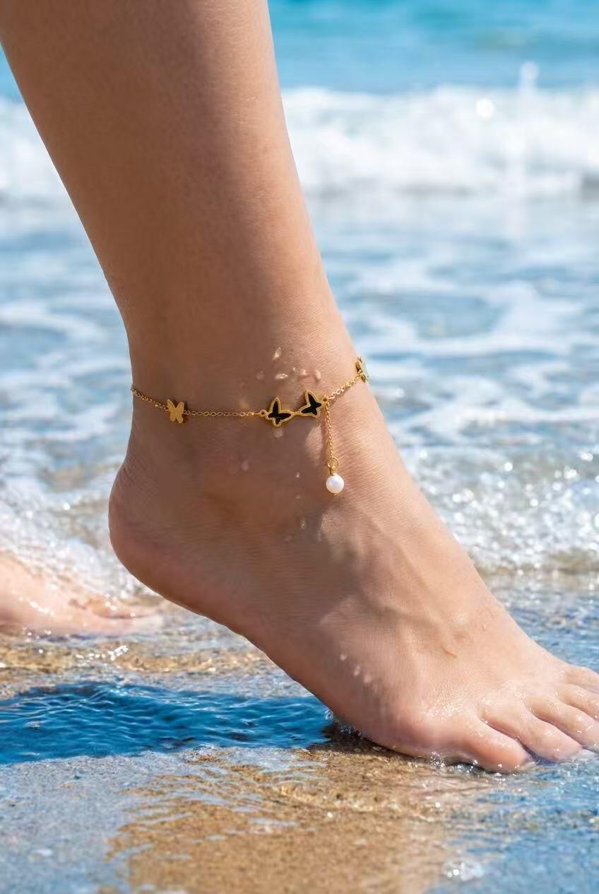 Grossista COSMOS - Cavigliera estiva da donna con ciondoli a farfalla e perla dorati, acciaio inossidabile alla moda