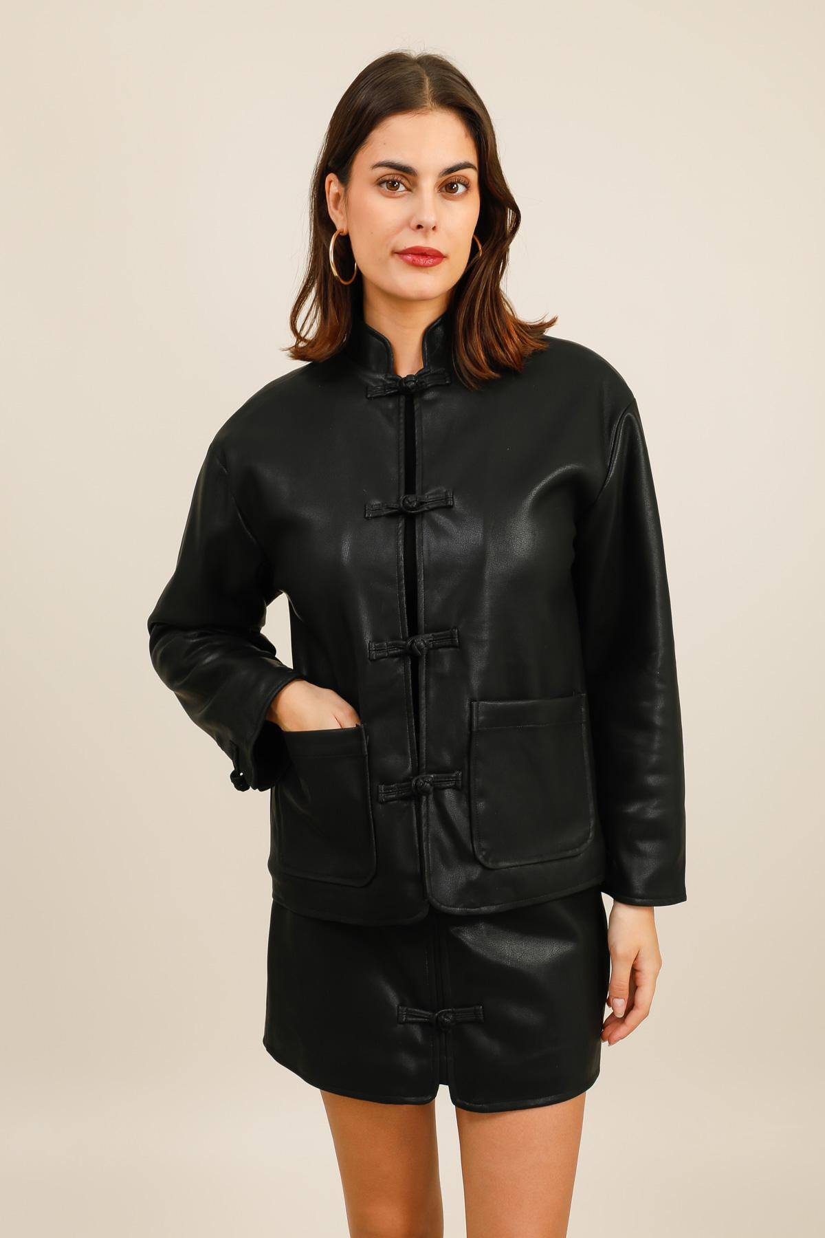 Blouson en similicuir à l’allure vintage.  Il présente une coupe droite et un col montant, fermé par des attaches nouées ton sur ton qui rappellent le style chinois traditionnel.  Deux grandes poches plaquées structurent le bas de la pièce.  La doublure en bouclettes apporte chaleur et confort, contrastant avec l’aspect lisse et structuré du similicuir.