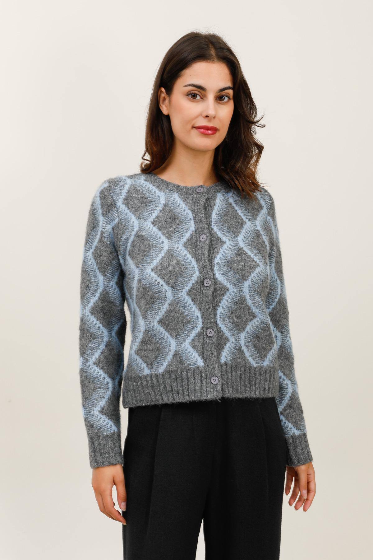 Gilet en maille duveteuse à motifs de vagues.  Il présente une coupe droite et un col rond, fermé par une rangée de boutons sur le devant.  Les bords côtelés à la base et aux poignets ajoutent une touche de structure et de confort.