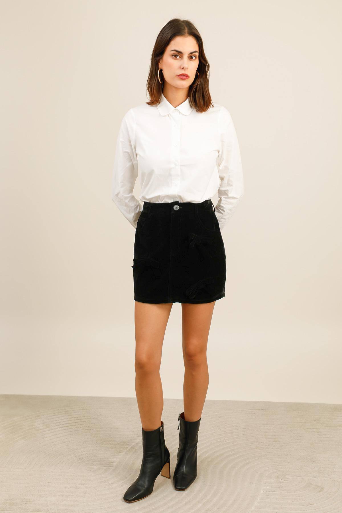 Jupe courte en velours au toucher doux.  Elle présente une coupe droite avec deux poches discrètes sur le devant et de jolis nœuds en velours ton sur ton, apportant une touche raffinée à la pièce.