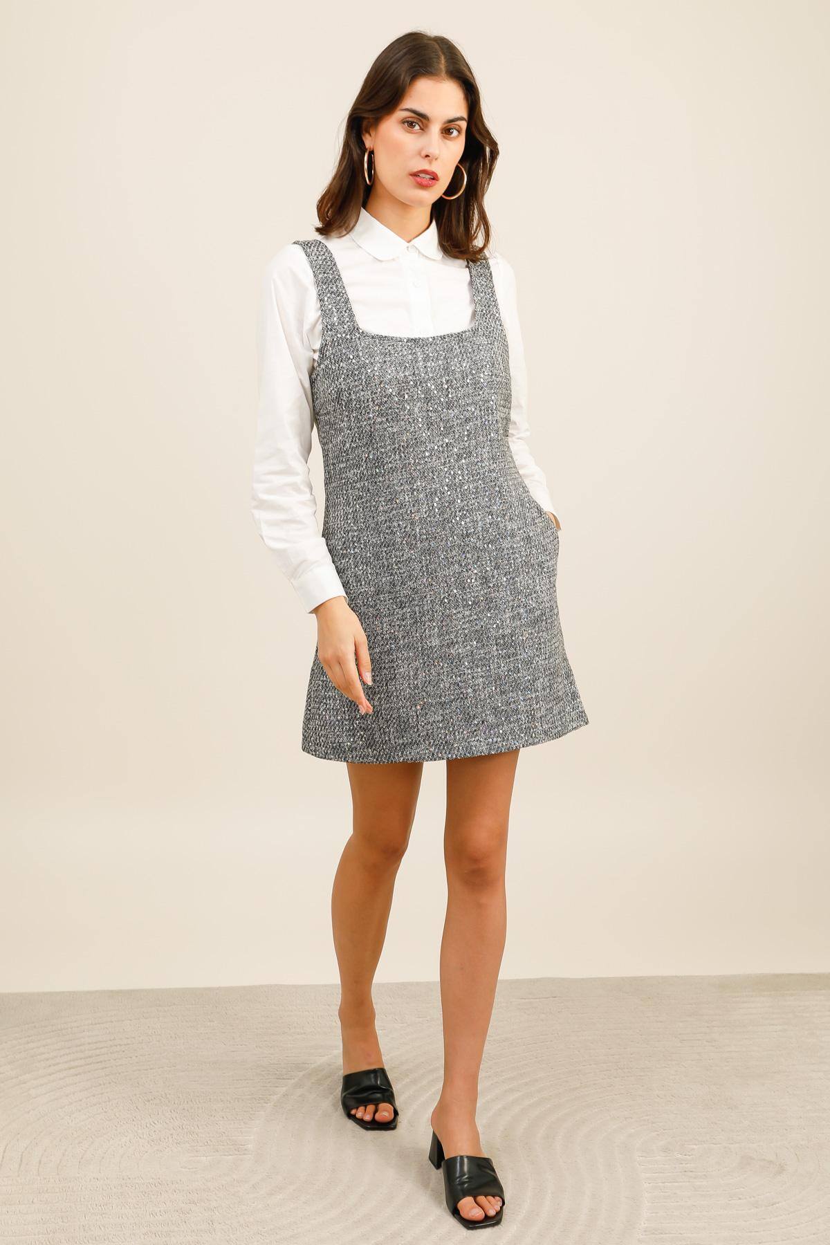 Robe courte en tweed parsemée de sequins subtils qui apportent une légère brillance au tissu.  Elle présente une coupe droite et un décolleté carré, soulignée par de larges bretelles pour une allure à la fois élégante et moderne.