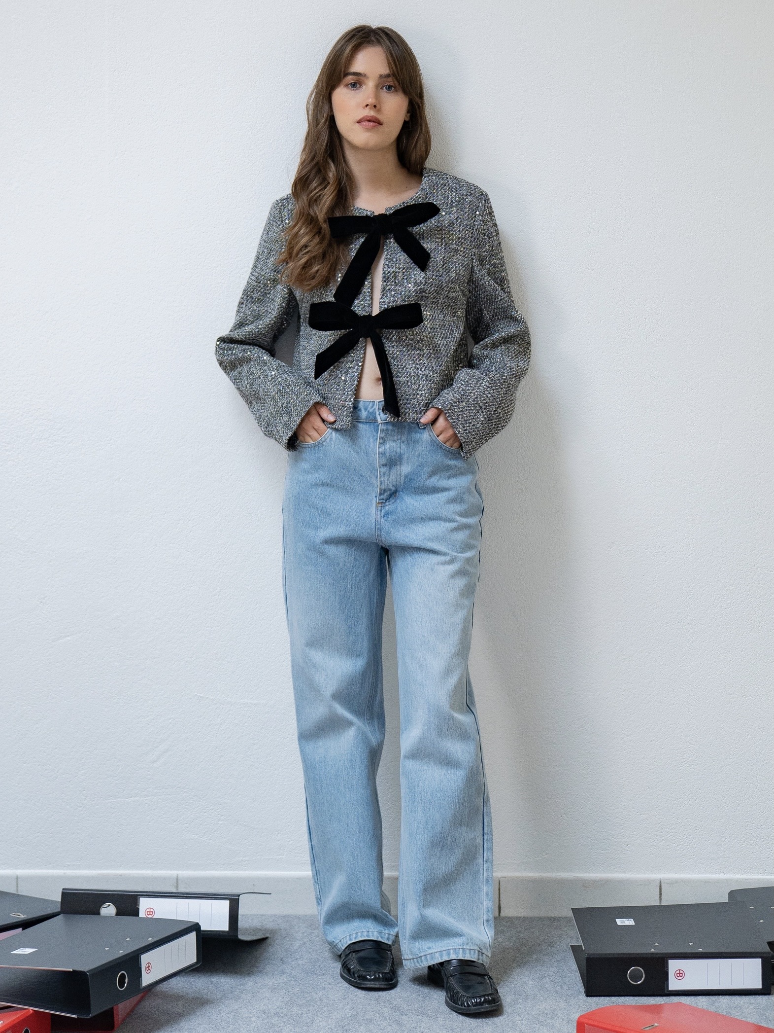 Veste courte en tweed parsemée de sequins discrets qui ajoutent une touche lumineuse et raffinée.  Elle présente une coupe droite et un col rond, fermée à l’avant par deux rubans en velours à nouer, pour un effet élégant et féminin.