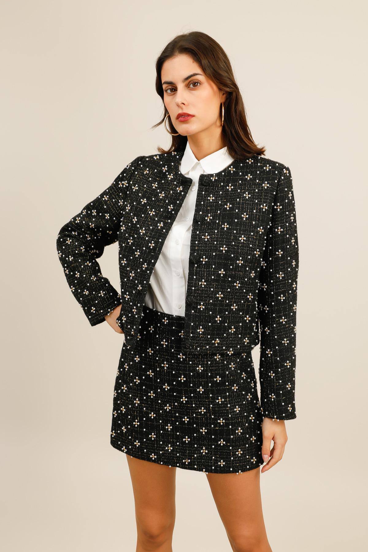 Veste courte en tweed noir rehaussée de perles et petites perles dorées disposées en motifs géométriques raffinés sur l’ensemble du tissu.  Elle présente une coupe droite et structurée, une encolure ronde et une fermeture par boutons recouverts de tissu pour un fini élégant.