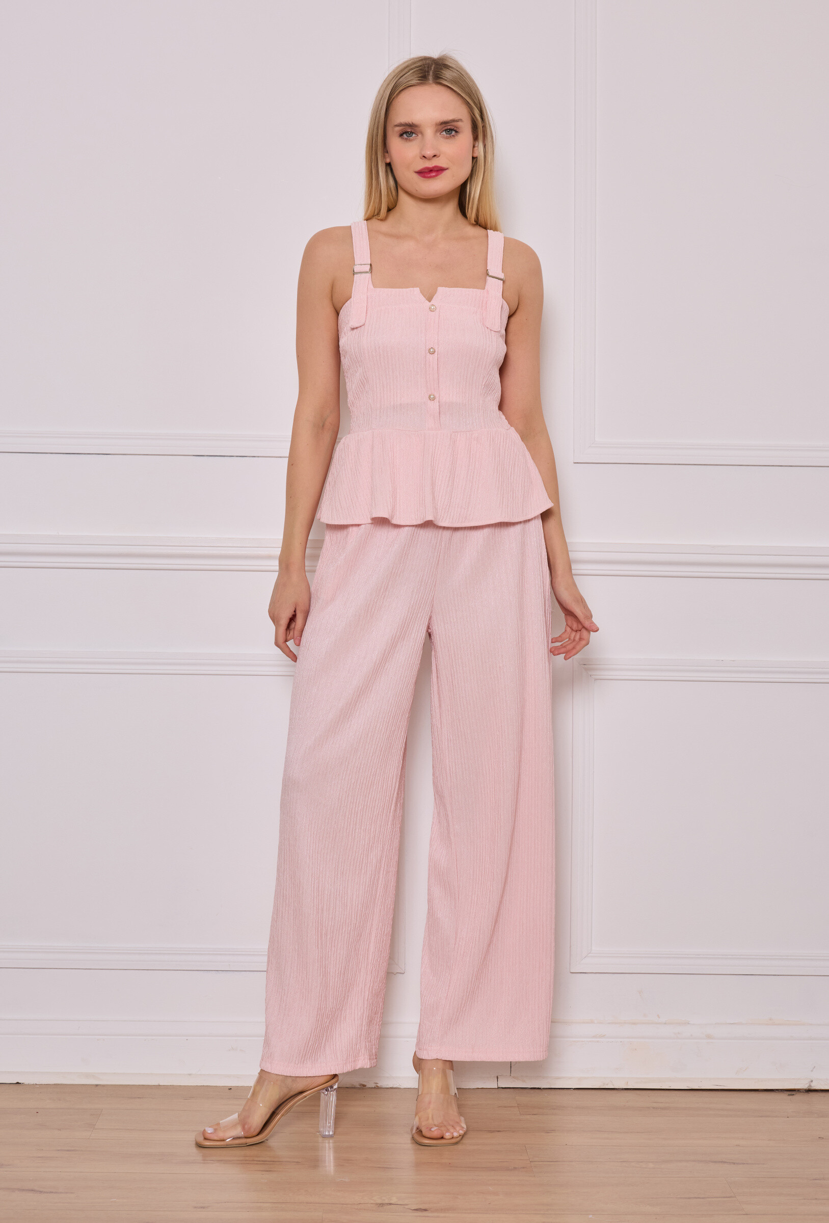 Cet ensemble rose clair associe féminité et confort avec un top à bretelles épaisses, boutons décoratifs et bas volanté, accompagné d’un pantalon large en tissu plissé. Une silhouette douce et élégante pour les beaux jours.