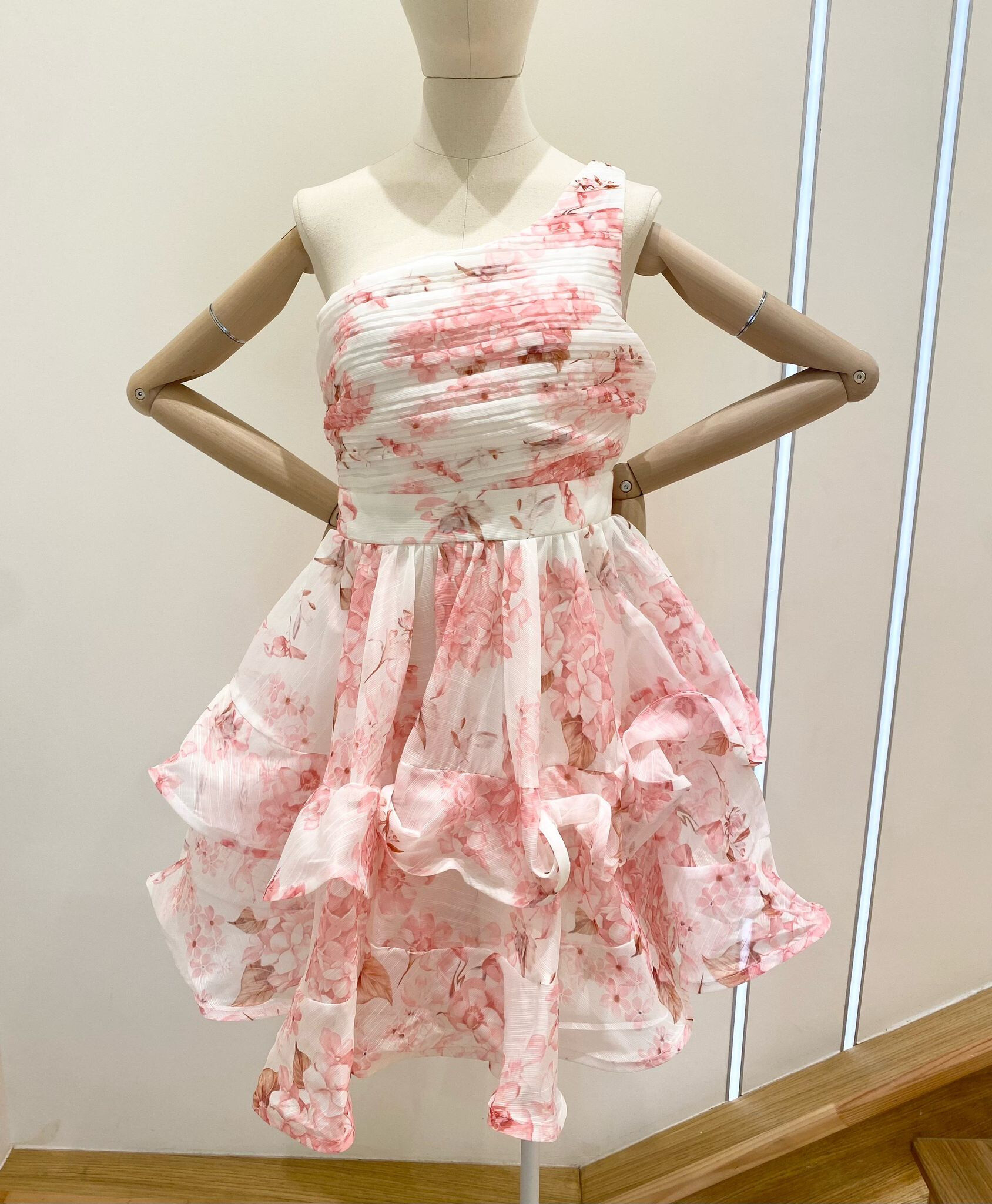 Craquez pour cette robe courte à l’allure romantique, dotée d’un élégant décolleté asymétrique et d’un bustier plissé. Sa jupe à volants superposés apporte volume et légèreté au mouvement. Imprimée de délicates fleurs roses, bleues ou jaunes, elle incarne la fraîcheur printanière idéale pour les occasions estivales.