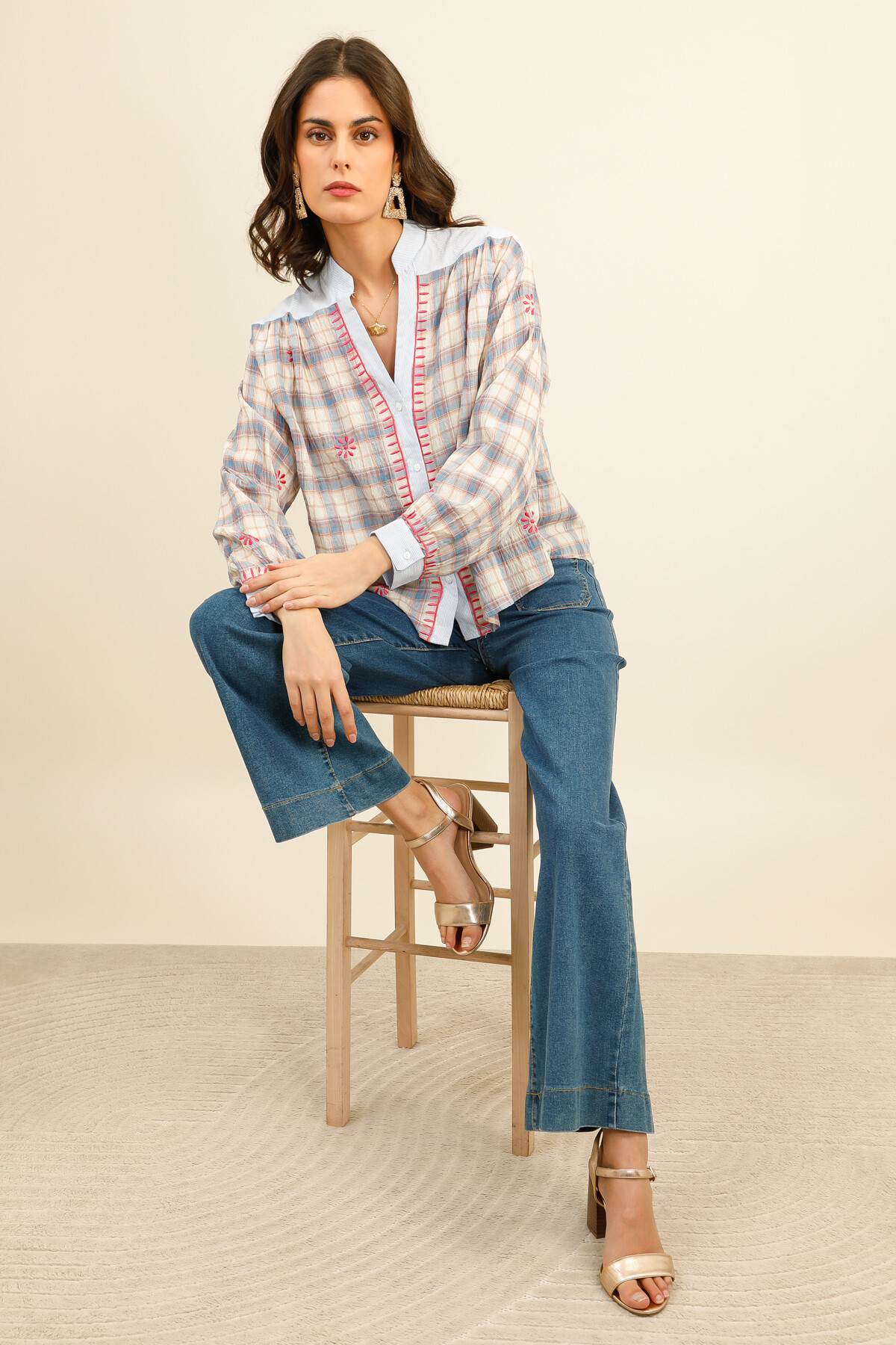 Grossiste Inspiration Studio - Blouse à carreaux en voile léger, broderies florales contrastées, finitions rayées bleu ciel et détails brodés rose framboise le long de l’ouverture.