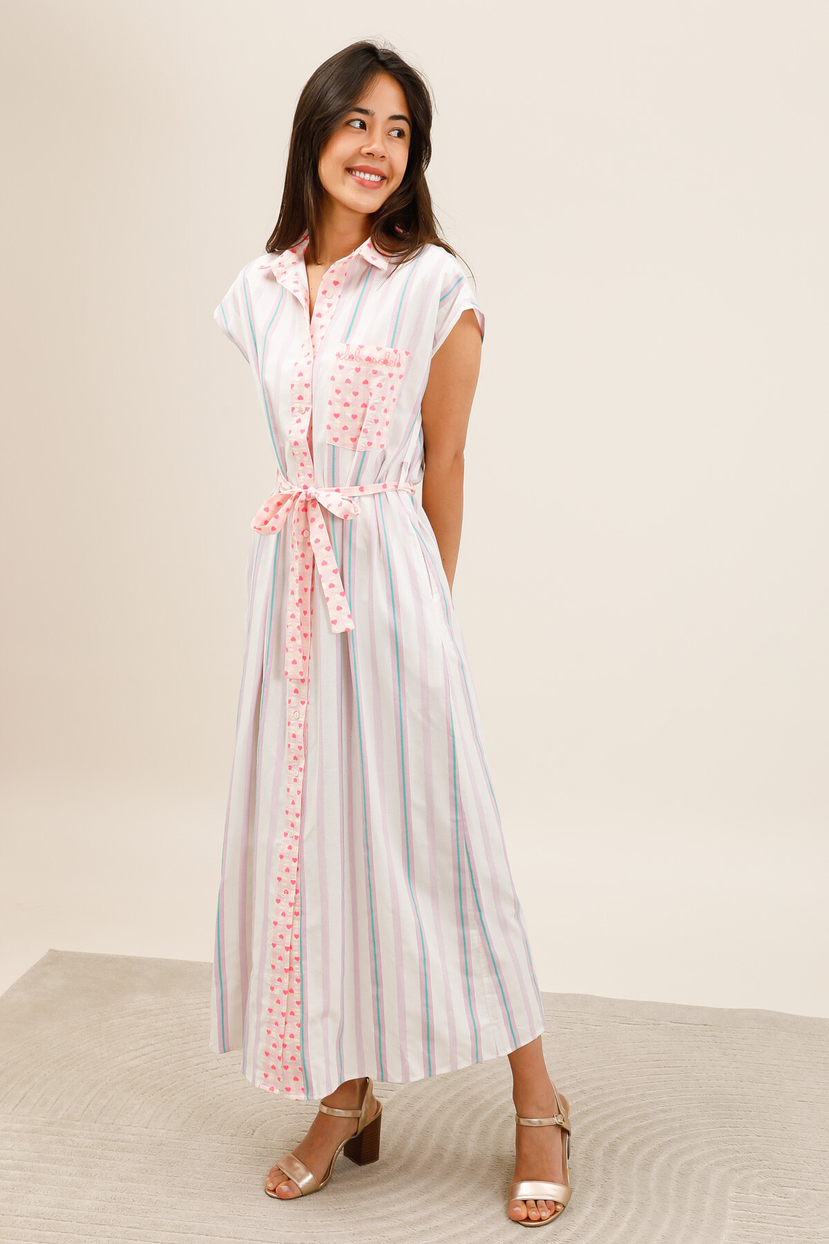 Grossiste Inspiration Studio - Robe chemise longue à rayures pastel, avec détails imprimé cœurs, ceinture à nouer et broderie “Club Soleil” sur la poche poitrine.