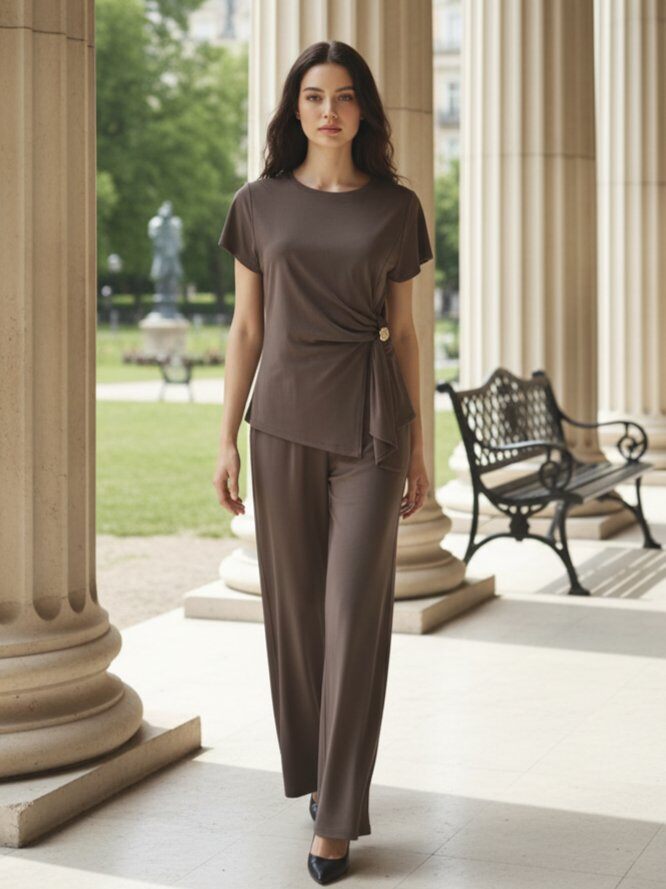 Grossista J&H Fashion - Completo coordinato fluido, composto da un top drappeggiato asimmetrico con maniche corte ornato da un bottone gioiello sul lato e pantaloni ampi a gamba fluida