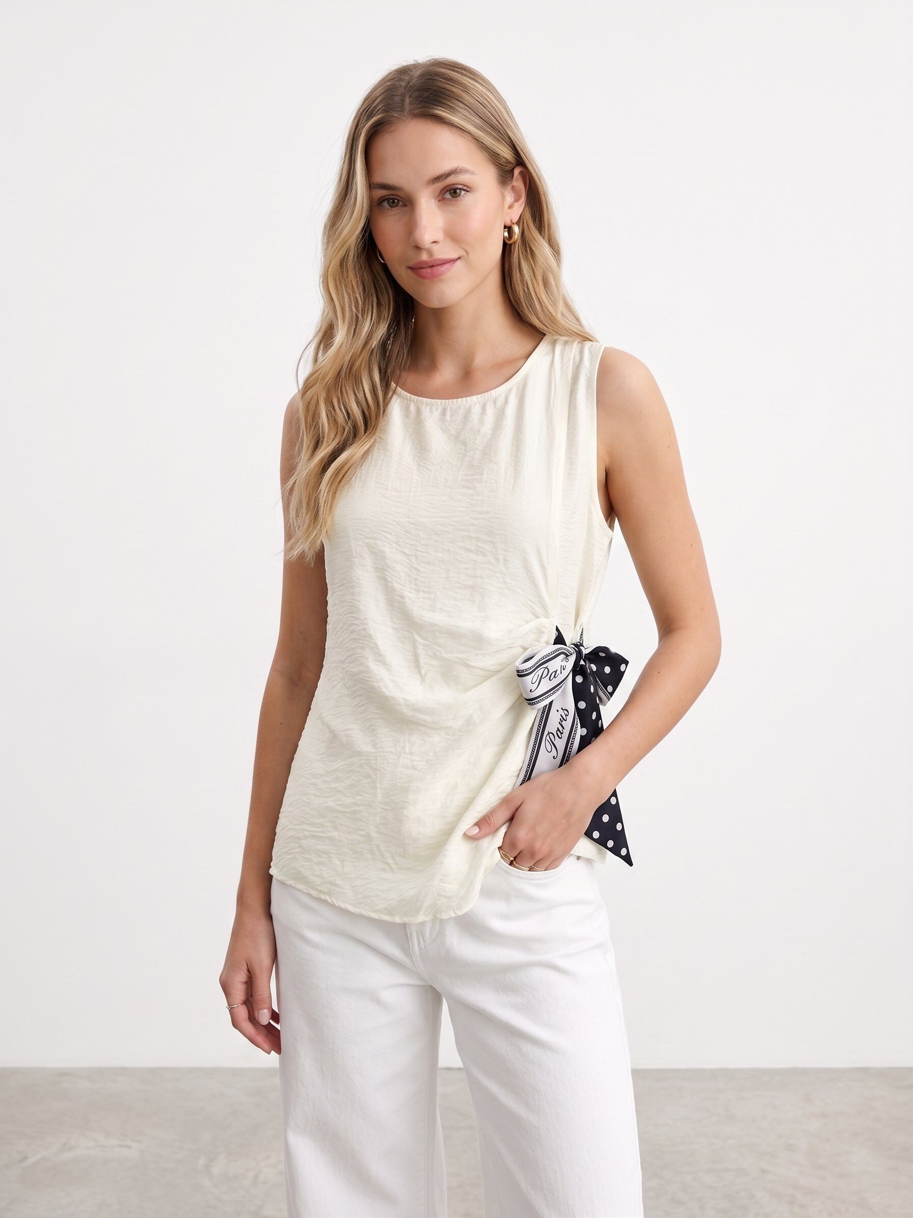 Grossiste J&H Fashion - Haut sans manches fluide présente une coupe asymétrique élégante, sublimée par un nœud latéral à pois au fini sophistiqué.