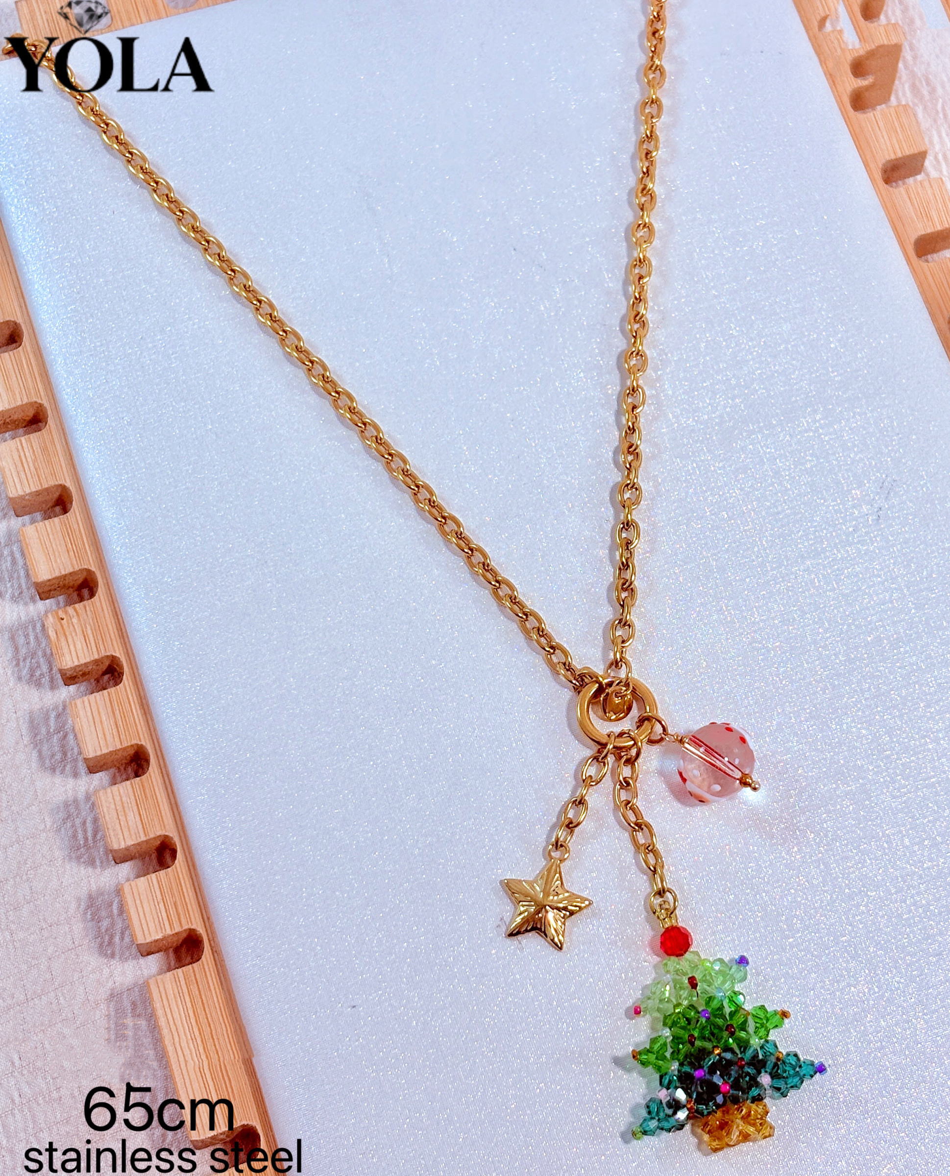 Wholesaler JESSICA - 这是一款金色水晶圣诞树吊坠长项链，材质为不锈钢，链长 65cm。项链采用细 O 字链设计，吊坠由金属五角星、琉璃圆珠和手工水晶串珠圣诞树组成，整体节日氛围比较强。款式精致可爱，适合圣诞节期间佩戴，也可以作为毛衣链使用。