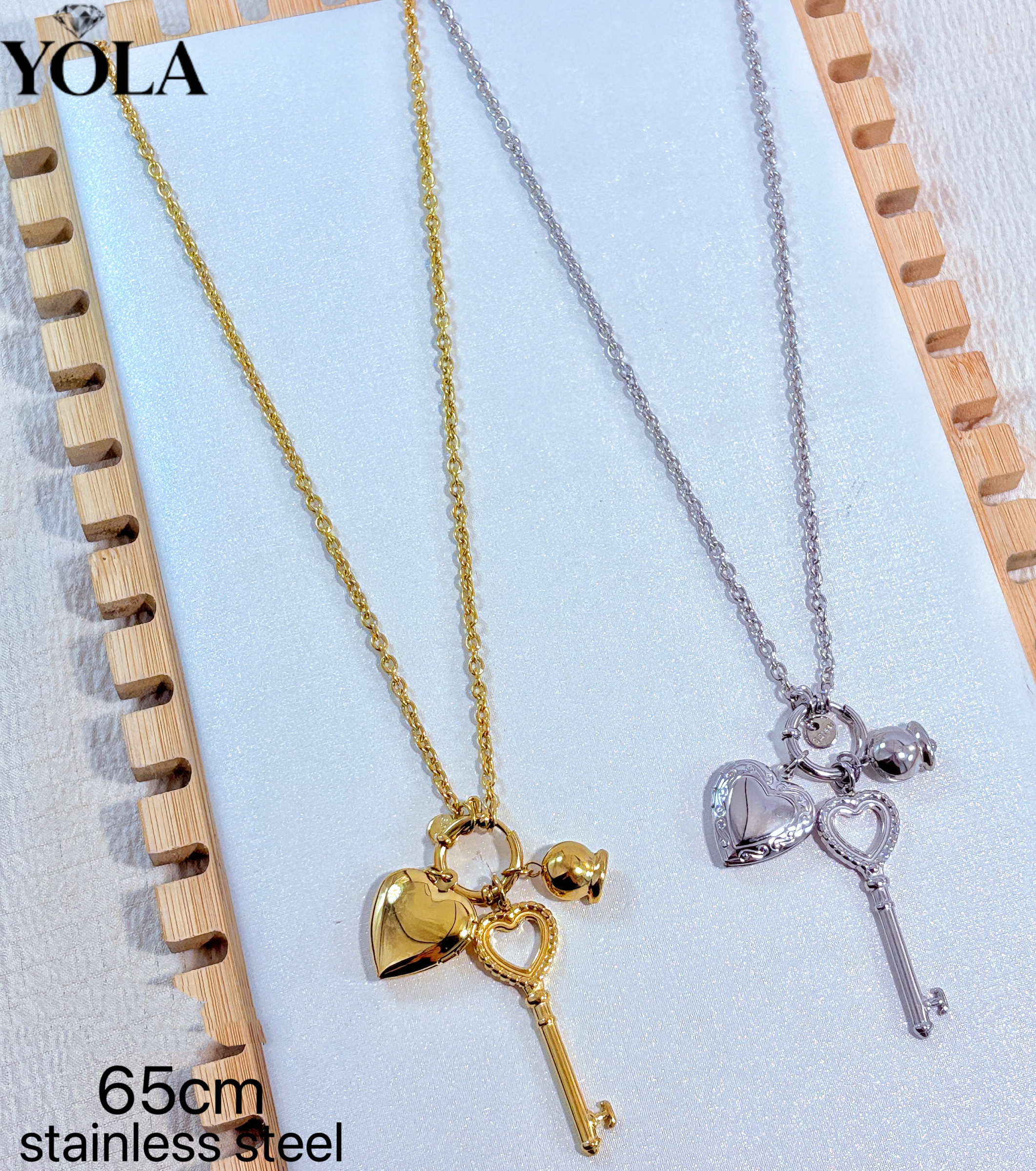 Wholesaler JESSICA - 这是一款爱心、钥匙、元素组合的长款项链，材质为不锈钢，链长 65cm。项链为细链设计，吊坠包含可打开的爱心相盒、镂空爱心、钥匙和小铃铛等元素，整体偏甜美复古风。金色款更温柔，银色款更清爽，适合搭配毛衣、衬衫等秋冬穿搭。