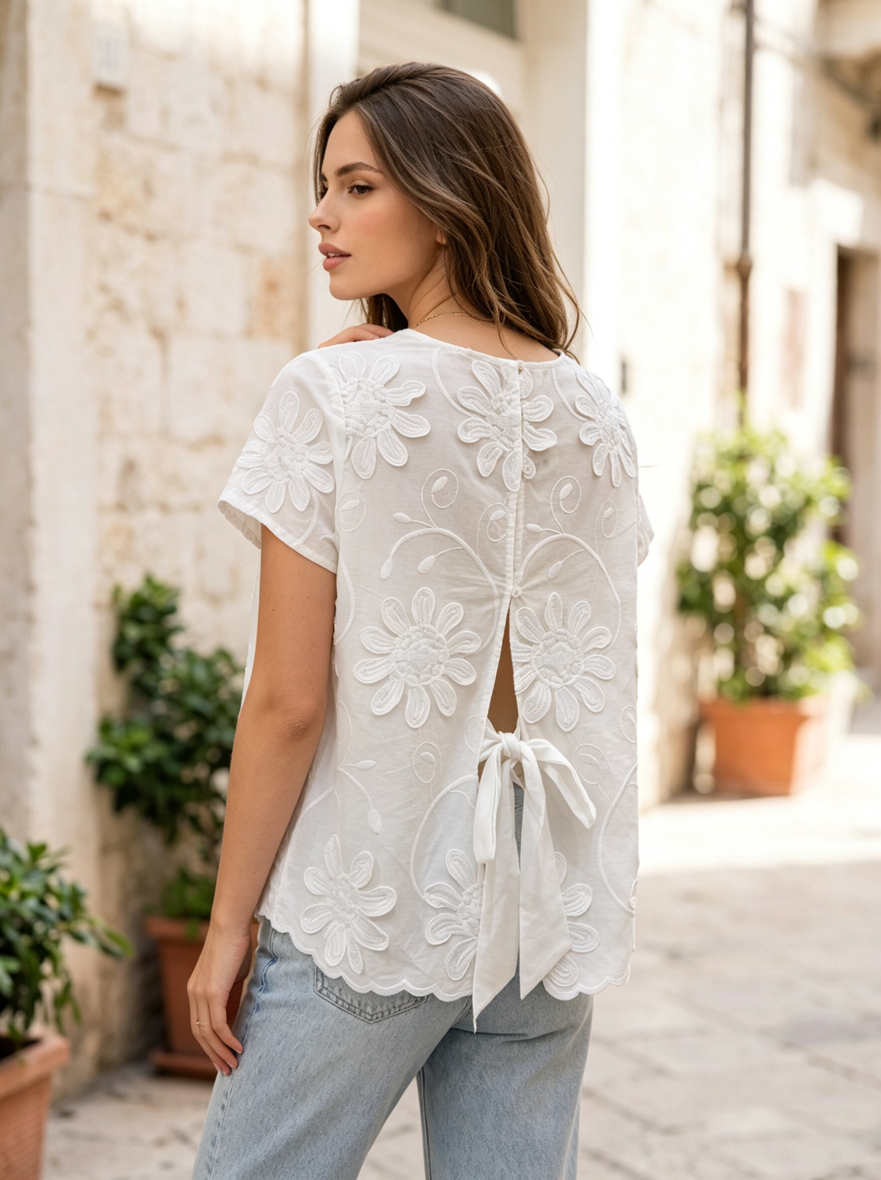 Grossista MYRACLEX - Una delicata blusa bianca ornata di ricami floreali in rilievo, con chiusura a bottoni sul retro e dettaglio da annodare