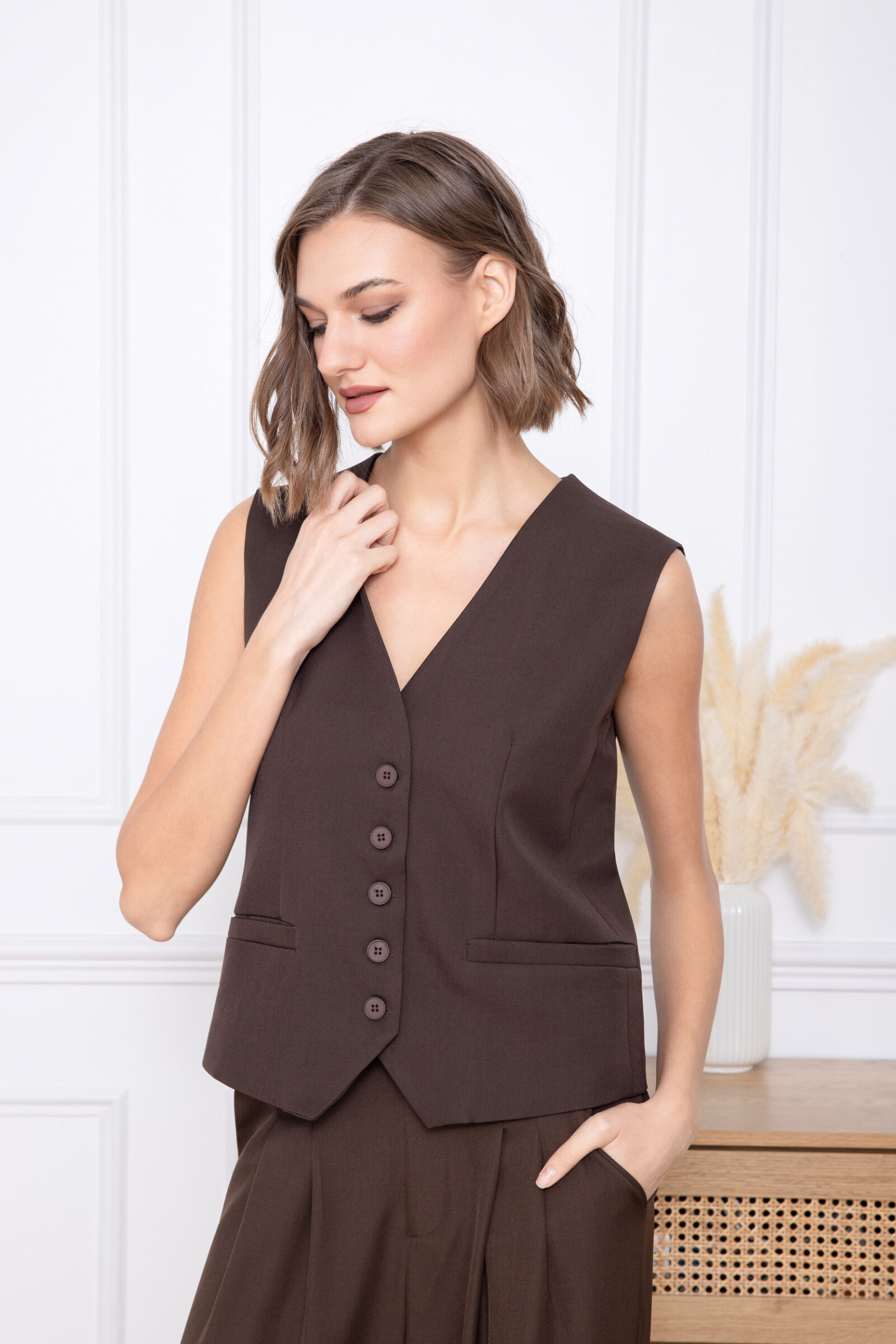 This sleeveless vest seduces with its fitted cut and its style inspired by modern tailoring. The V-neckline highlights the bust while providing an elegant and feminine touch. The buttoned front closure structures the silhouette, while the welt pockets add a neat and functional finish. The back is delicately worked with a discreet tightening tab for an optimal fit. Made from a fluid and comfortable material, this cardigan is ideal for creating refined looks, both worn alone or as a coordinated ensemble.