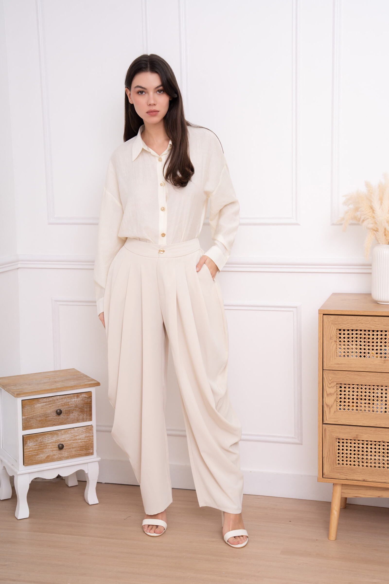 Pantalon à coupe large et structurée, avec taille haute soulignée par une ceinture lisse et un bouton décoratif discret. Plis profonds à l’avant apportant du volume et un tombé fluide qui allonge la silhouette. Le bas légèrement resserré crée un bel équilibre entre élégance et modernité. Confection soignée dans un tissu souple offrant confort, aisance de mouvement et allure raffinée, idéal pour des looks chics comme plus habillés.