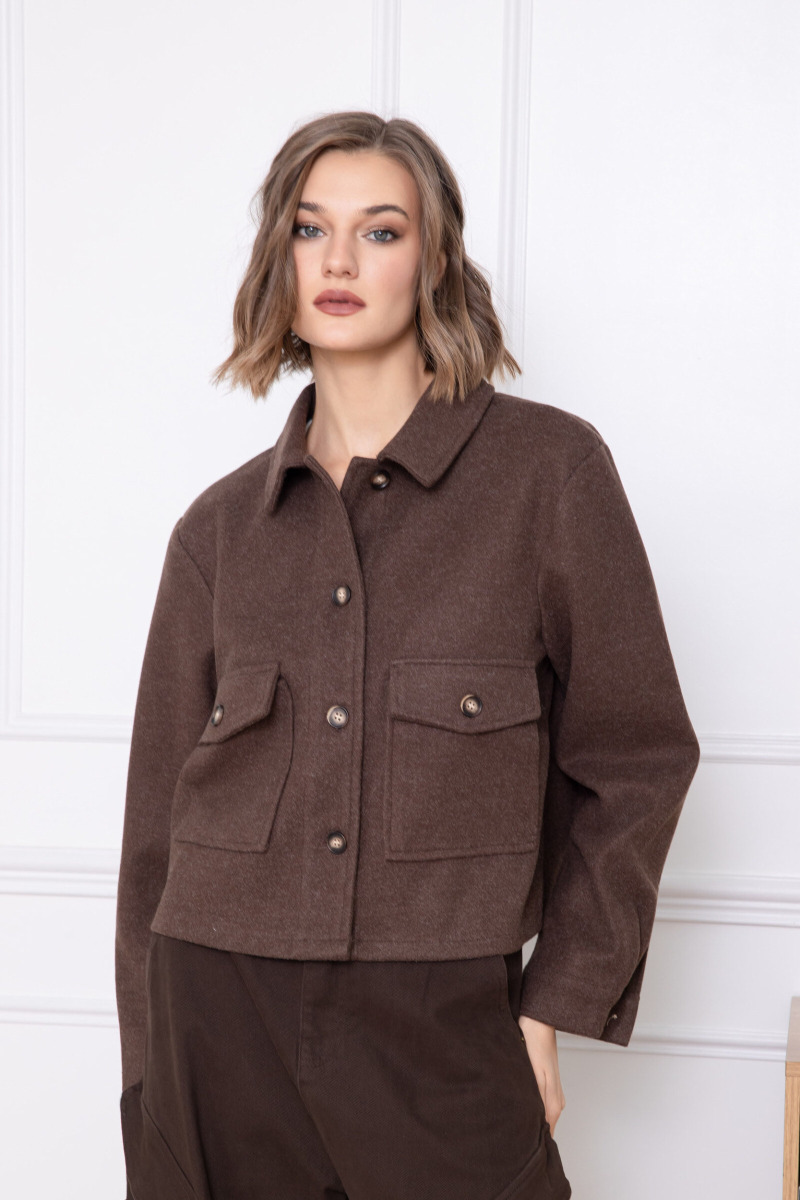 This short jacket is distinguished by its straight and structured cut, offering an elegant and contemporary look. Made from a soft and slightly textured material, it ensures optimal comfort while maintaining a clean drape. The classic collar adds a timeless touch, while the buttoned front closure reinforces its refined style. The patch pockets add a practical and aesthetic dimension, and the long sleeves slightly tightened at the wrists guarantee a harmonious fit. A versatile piece, ideal for putting together neat everyday or professional outfits.